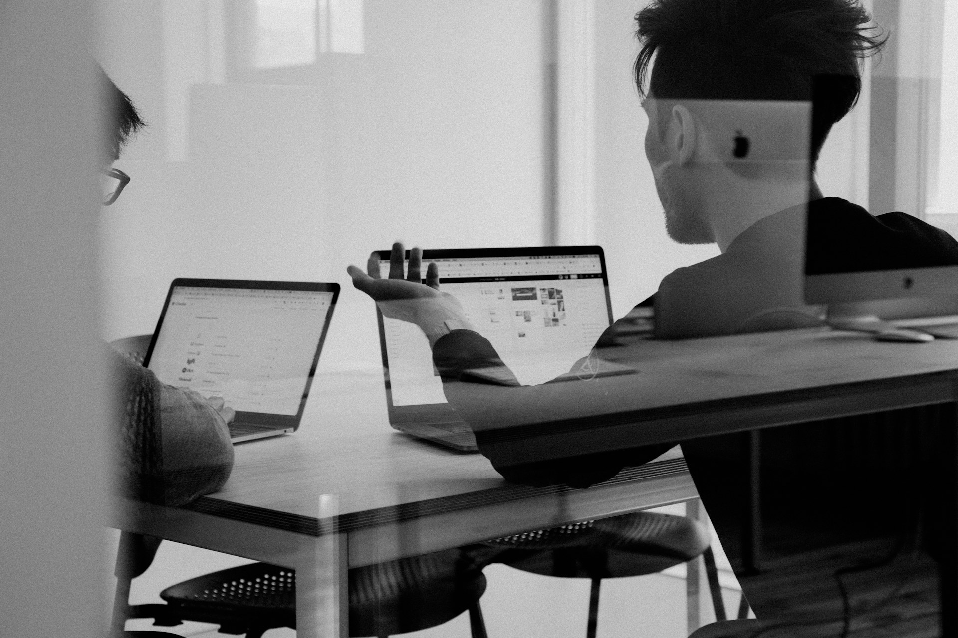 Zwei Personen besprechen ihre Arbeit an Laptops in einem Büro.
